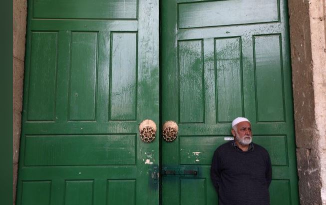 رجل يقف أمام أبواب مسجد الأقصى المغلقة يوم 15 مارس 2020. تصوير: عمار عوض - رويترز.